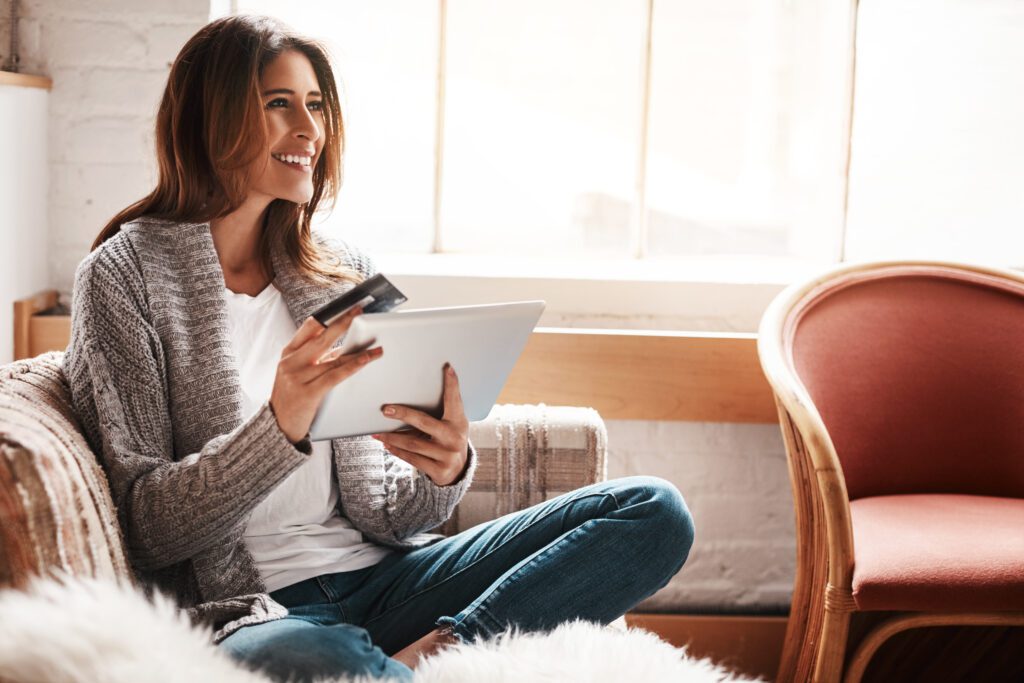 Shot of an attractive young woman using a digital tablet and credit card on the sofa at home